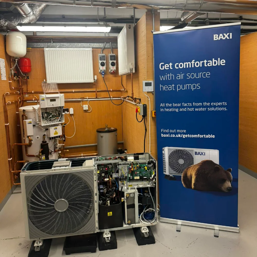 Baxi air source heat pump training display with an outdoor unit showing its internal components, alongside heating system equipment.