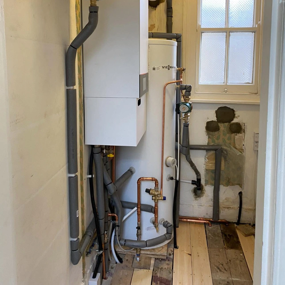 Wall-mounted heating boiler installed alongside a Viessmann hot water cylinder, expansion vessels and insulated pipework.