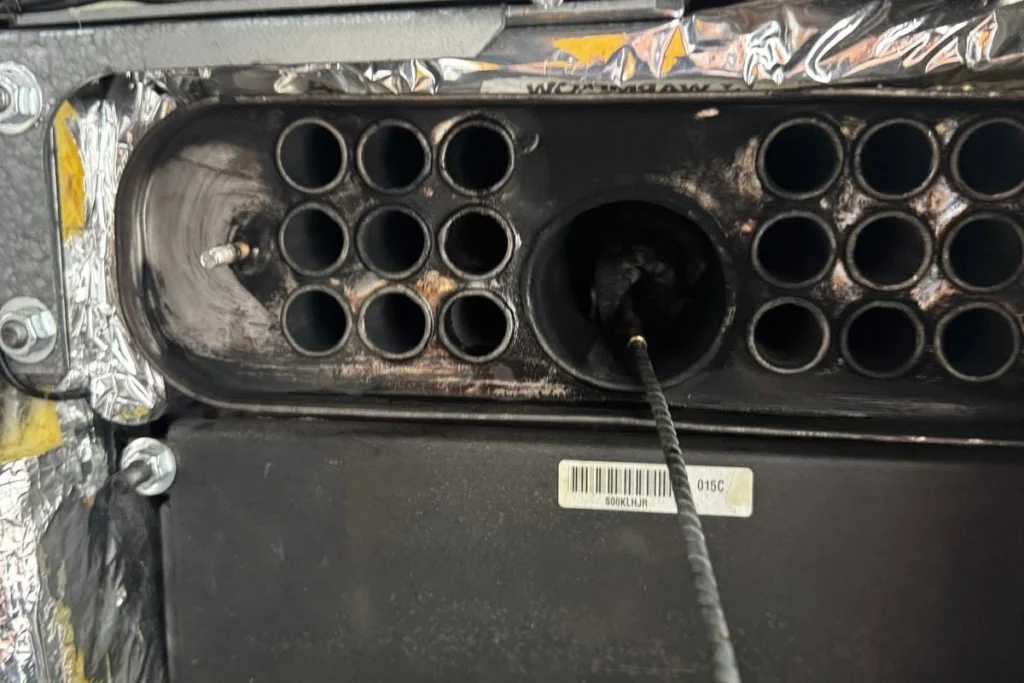 Close-up of an exposed boiler heat exchanger with metal tubes and a cleaning brush inserted during maintenance.