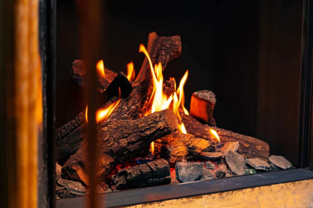 Burning logs with bright orange flames inside a modern black fireplace.