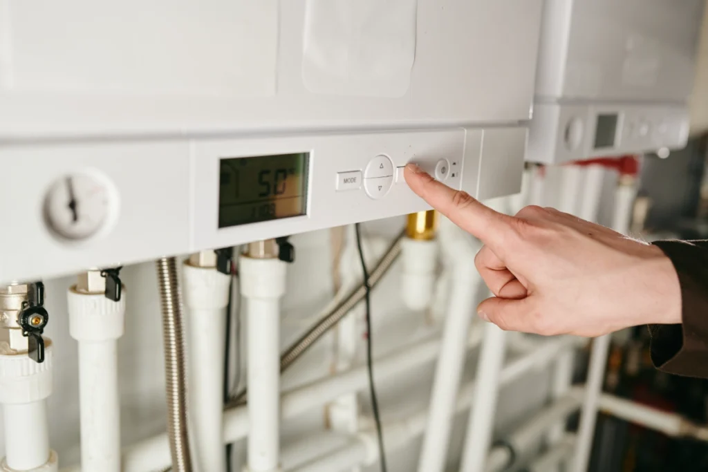 Person adjusting the temperature settings on a wall-mounted gas boiler using its digital control panel.