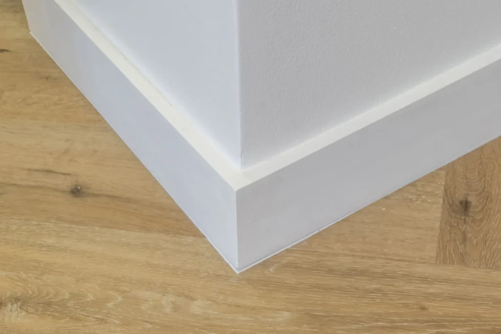 Plain white skirting boards fitted around an external wall corner above light oak-effect flooring.