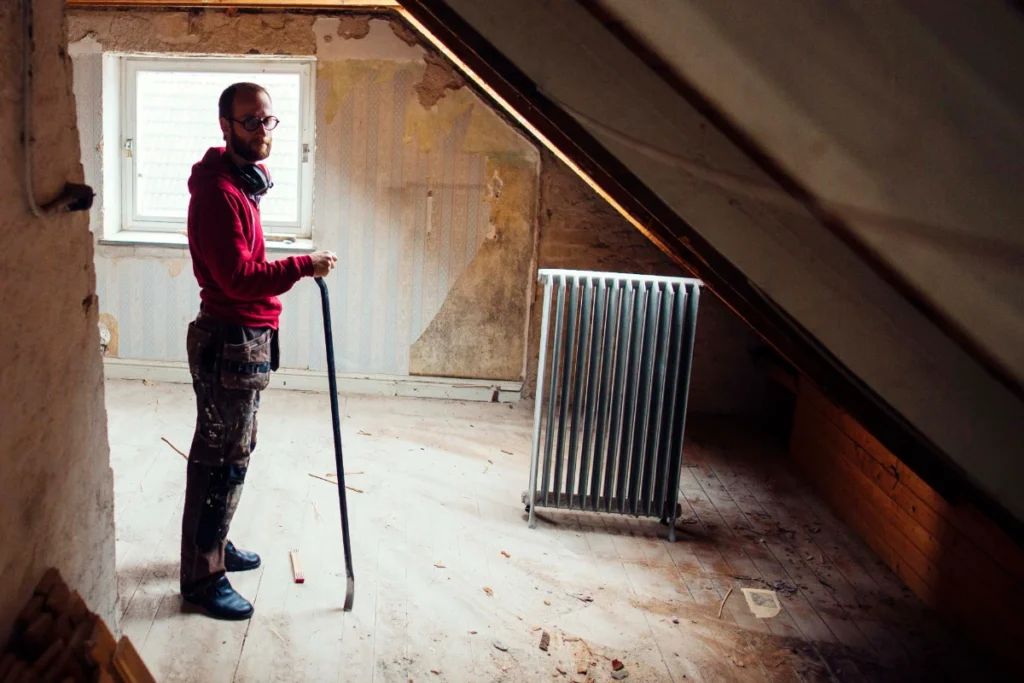 Man holding a pry bar inside an unfinished attic during a residential loft renovation.