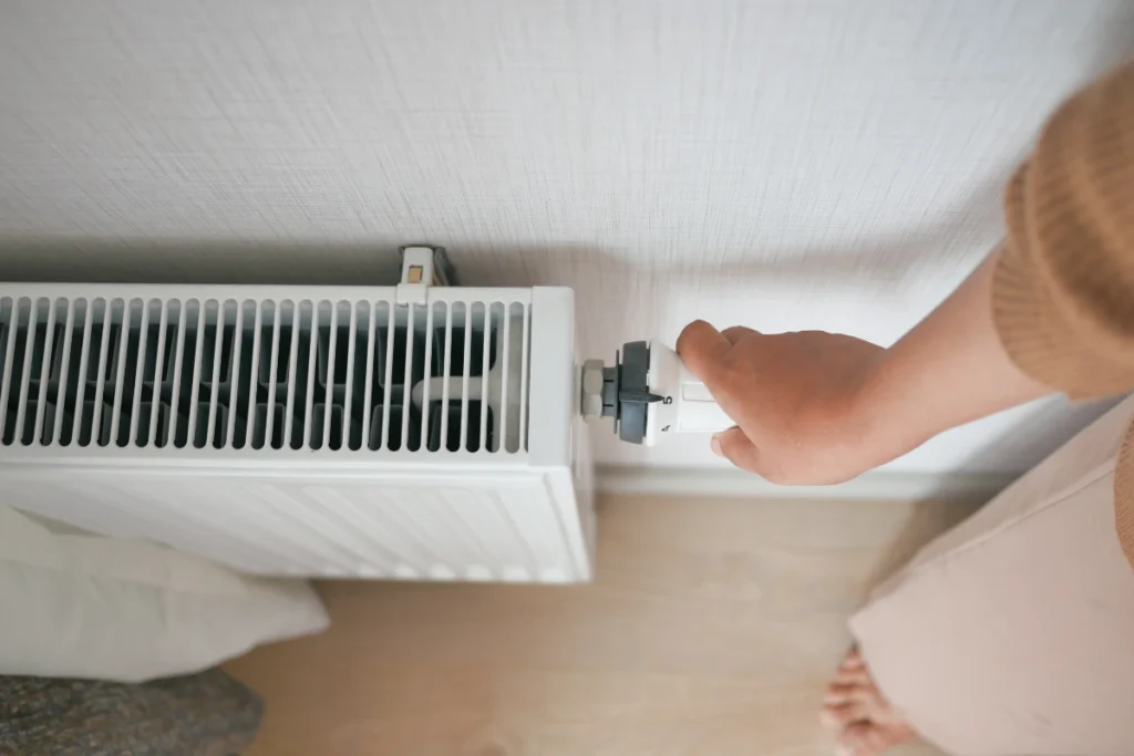Person adjusting a thermostatic radiator valve to control the temperature of a home heating system.